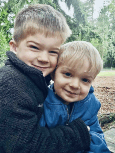 Two young boys smile for the camera. The boy on the left has short brown hair and wears a black fleece. The boy on the right has short blonde hair and wears a royal blue jacket. 
